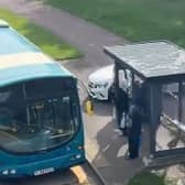 A screenshot from a video showing the driver on the footpath near a bus and bus stop full of passengers